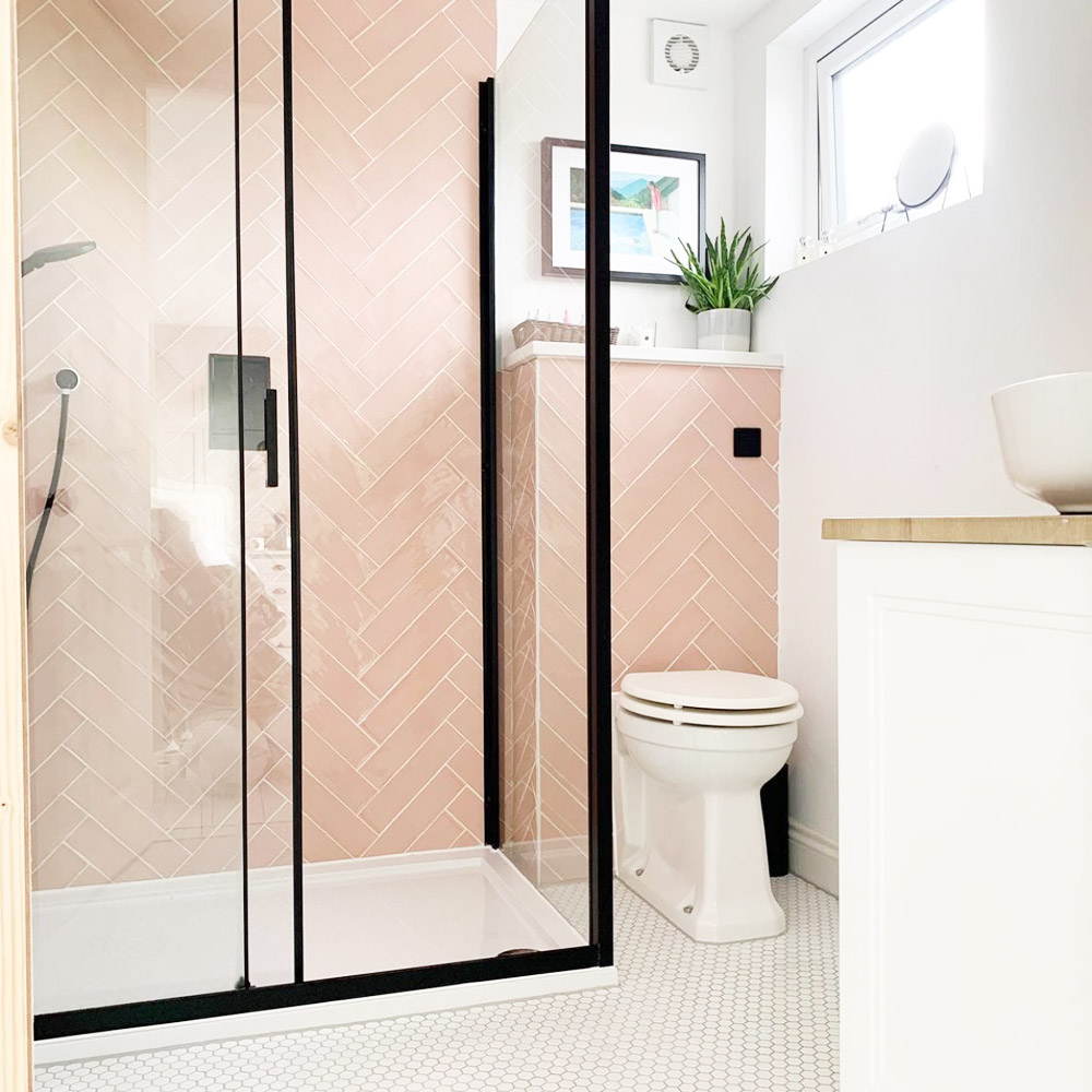 White bathroom with pink tiled shower area and black metal hardware. 