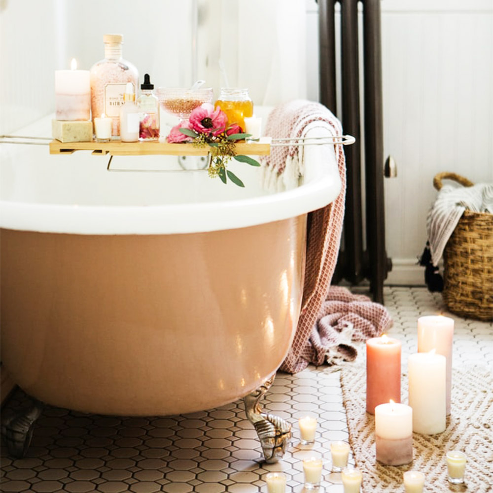 bath tub with flowers and bath products, and candles around the floor. 