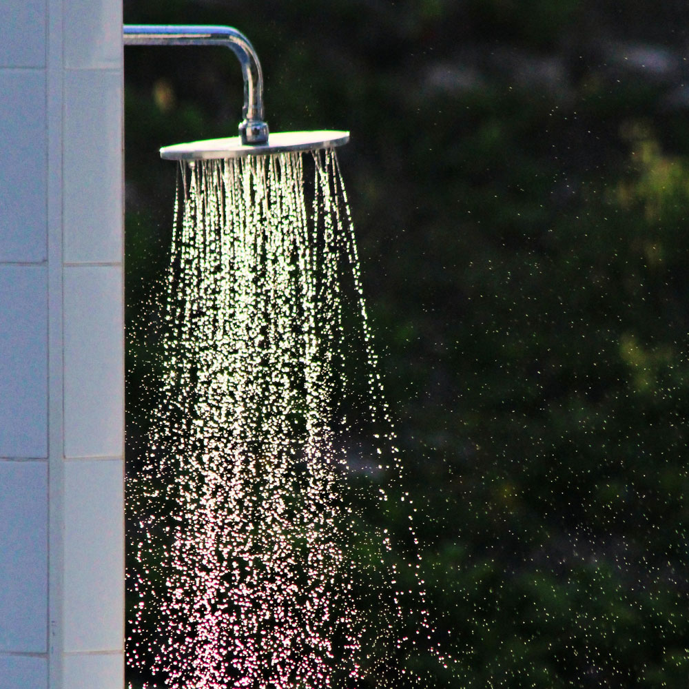 Outdoor chrome shower head running shower water.