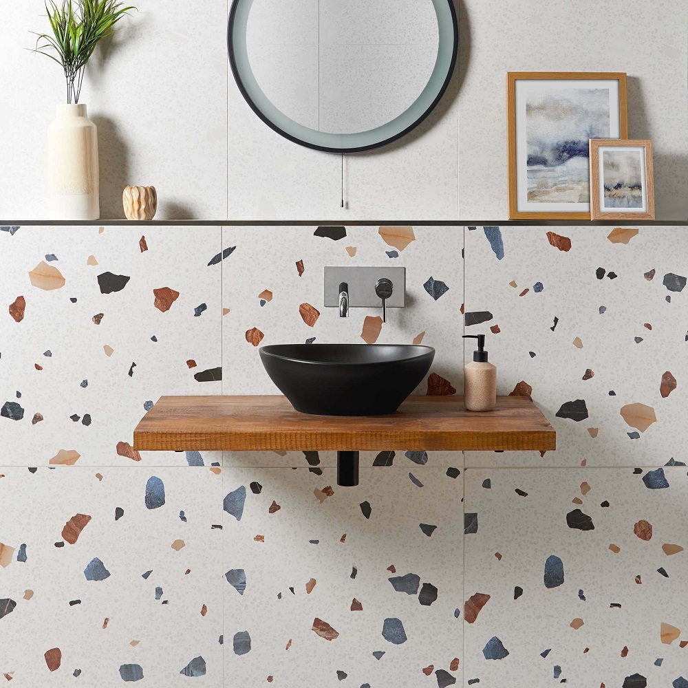 the bathroom has terrazzo tiles on the walls and a wooden shelf for a matt black sink.