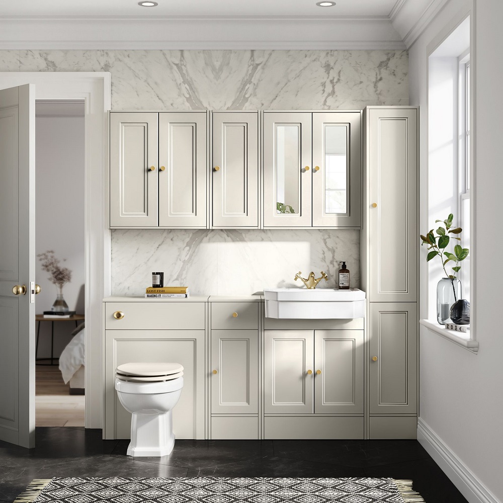 Elegant bathroom featuring cream panelled cabinetry with gold handles, a marble backdrop, pristine white sink with gold taps, and subtle decor touches like plants and a monochrome rug.