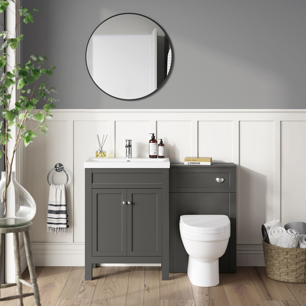 Chic bathroom space with a muted grey theme, featuring a round mirror reflecting white interior, grey vanity unit with personal care items, a tucked-away toilet, and a cosy corner adorned with a lush potted plant and striped towel.