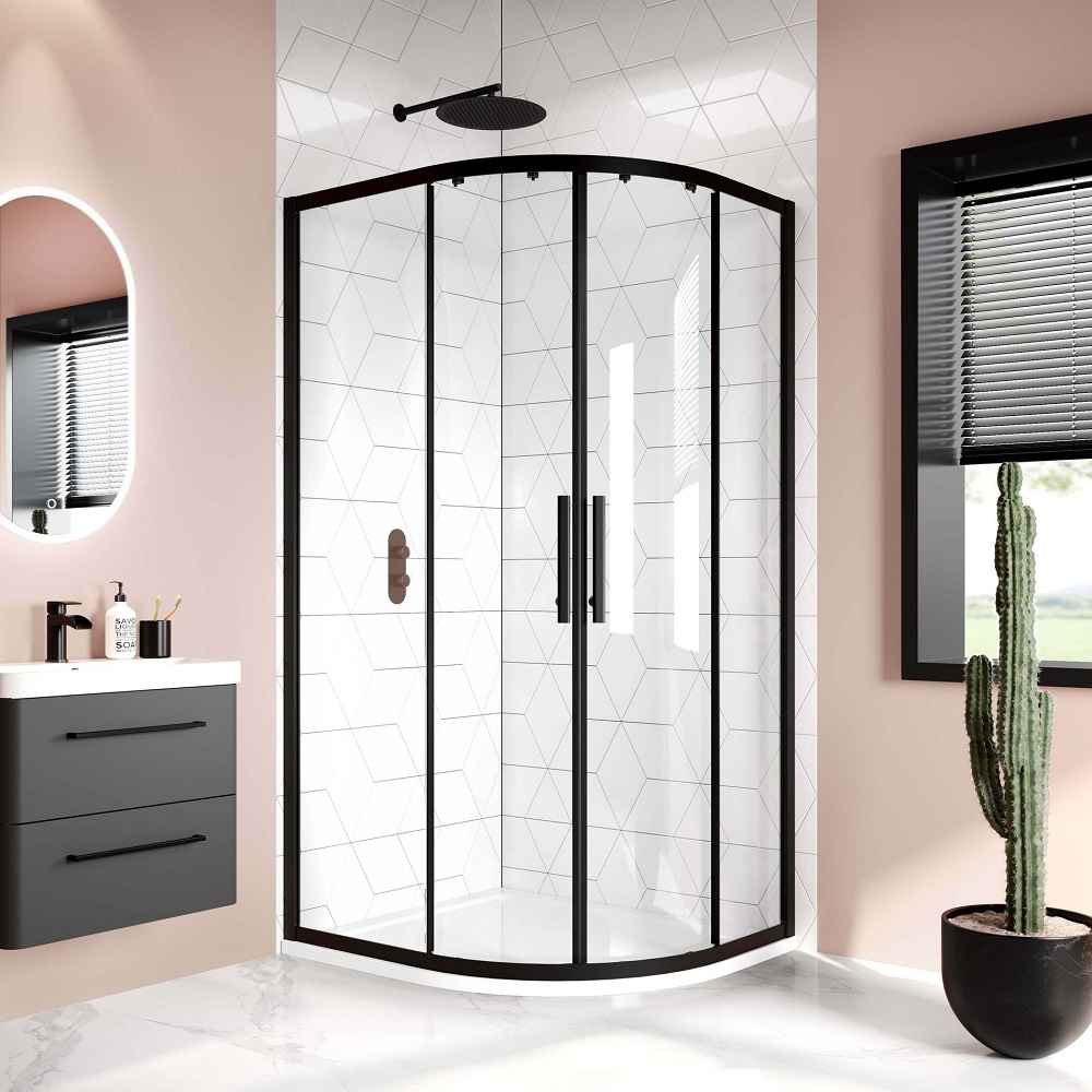 Contemporary bathroom with a curved glass shower enclosure, black frame details, and geometric wall tiles. A grey vanity cabinet and mirror with backlighting on the left, and a tall cactus plant in a pot add a unique touch.