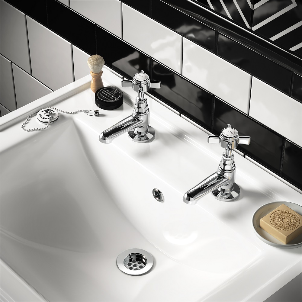 A close up of a white bathroom sink with traditional chrome basin taps, set against a backdrop of black subway tiles. A shaving brush, soap, and vintage bath plug rest on the sinks surface, enhancing the classic and sophisticated style. 