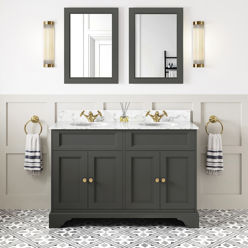 A classic bathroom setup with graphite grey double basin vanity, featuring a white marble top and two undermount basins. The gold faucets complement the vanity's gold knobs. Two framed mirrors are mounted above the vanity, flanked by vertical gold light fixtures. To the sides, gold towel rings hold striped black and white towels. The floor is tiled with a geometric black and white pattern, adding to the rooms elegant aesthetic. 