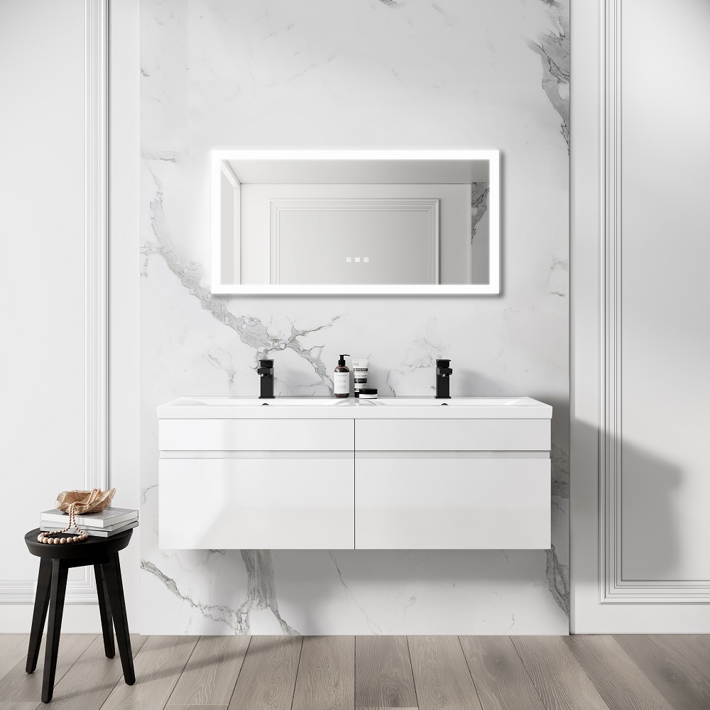 A minimal bathroom with a white floating double basin vanity, an illuminated LED mirror with a Bluetooth speaker, and a small black side table. The backdrop is a marble wall, and the floor is a light wood. 