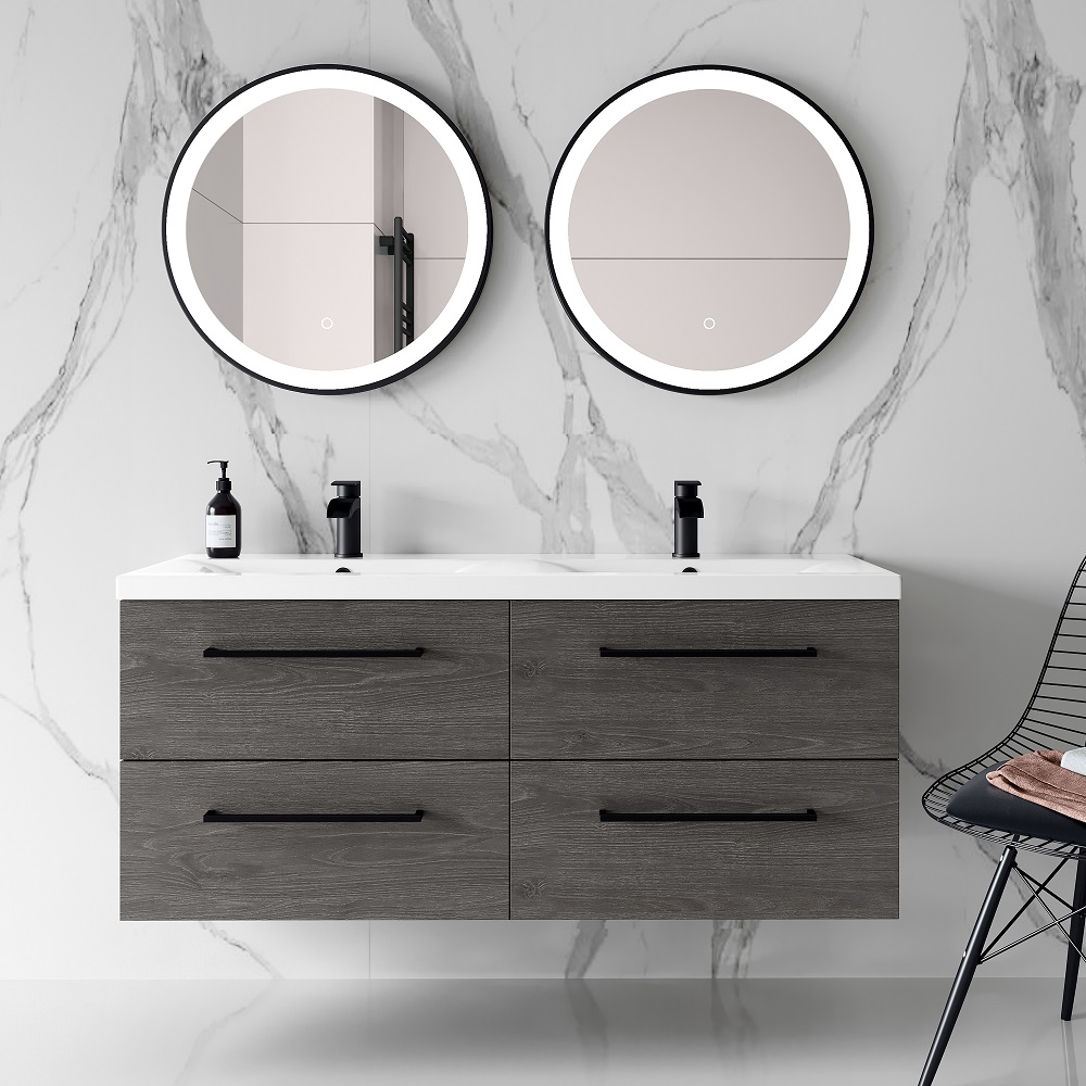 A contemporary bathroom with a charcoal elm double wall-hung basin vanity unit featuring clean lines and a white countertop. Above the vanity are two round mirrors with illuminated edges. On the vanity surface, black bottles add a contrast to the neutral tones, and to the side, a black wire chair and a pink towel introduce a subtle colour accent. The backdrop is a marble wall with dramatic veining, and the flooring is a light, natural wood. 