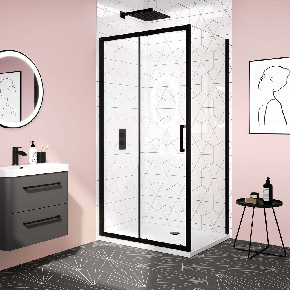 A modern bathroom with a matt black sliding shower enclosure, white geometric patterned tiles inside, and dark geometric floor tiles. There's a floating grey vanity with a white countertop and black faucet, a round mirror with a black frame, and line art wall decor. A side table holds bath products, adding to the clean and contemporary design. 