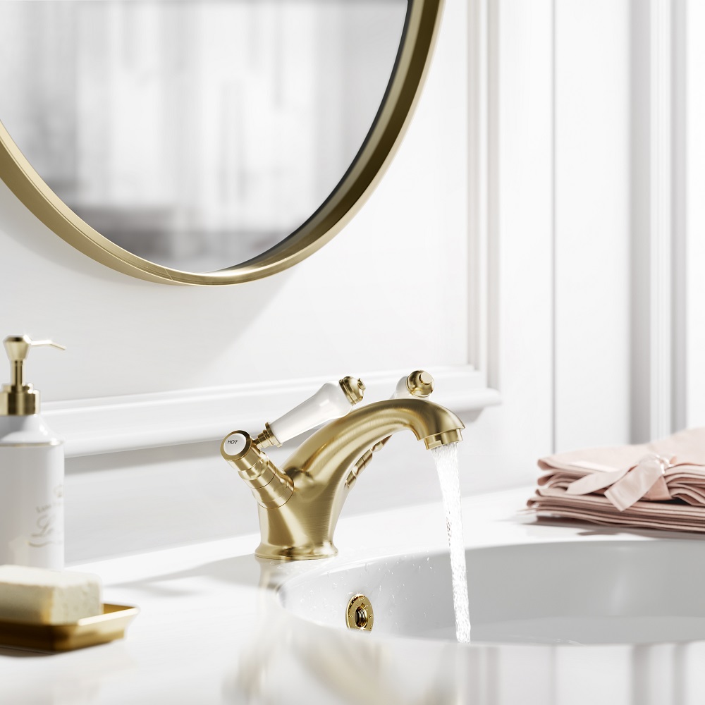 Elegant brushed brass basin mixer tap with a classic design, mounted on a white pedestal sink. A luxurious touch for any bathroom, complemented by a round gold-framed mirror and crisp white wainscoting. Perfect for adding a hint of vintage charm to a modern space. 