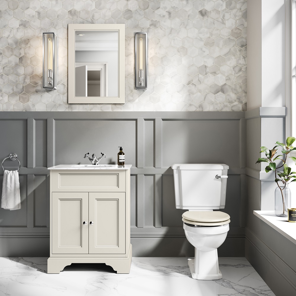 Chalk white bathroom vanity cabinet with a classic style, paired with a white framed mirror, flanked by elegant art deco wall sconces. The space features a hexagonal tile backsplash, grey wainscoting, and a simple white toilet, creating a harmonious blend of traditional and contemporary design elements. 
