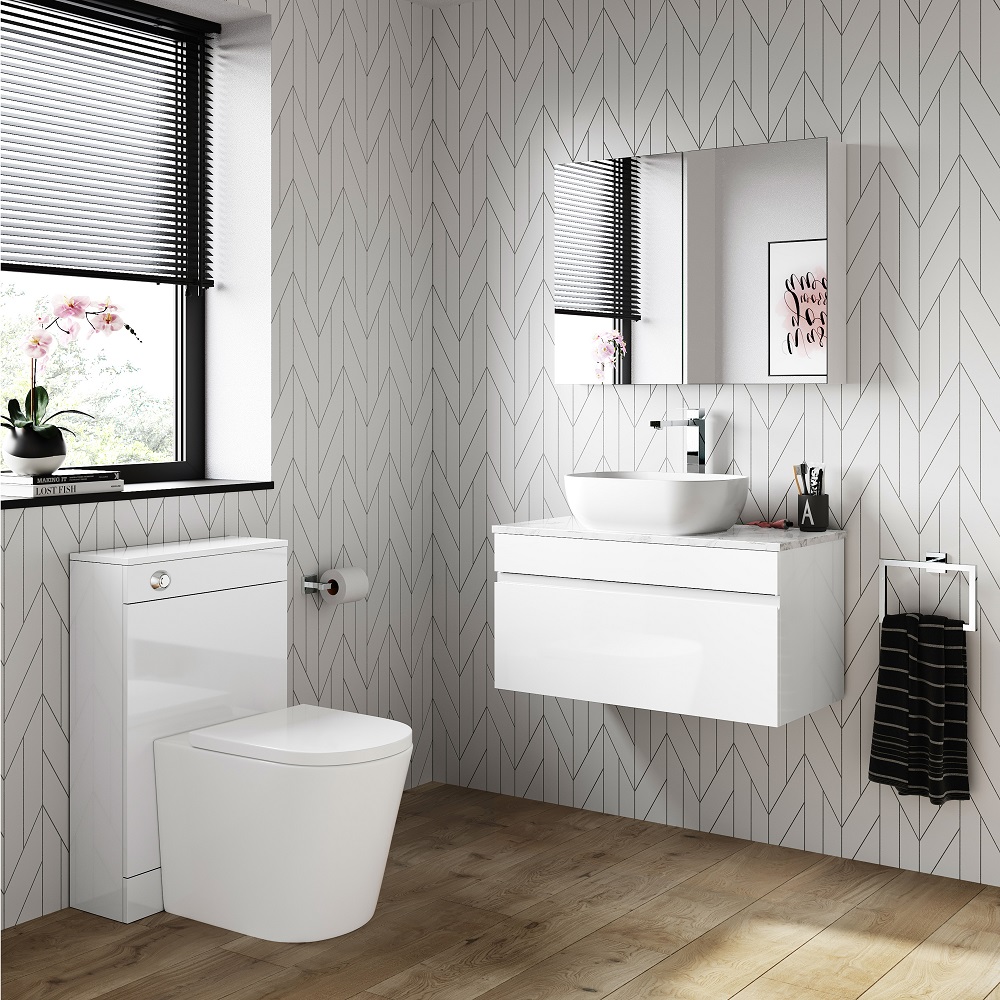 A contemporary white wall-hung vanity unit with a marble top and a vessel sink, set against a geometric patterned herringbone wall in a monochrome palette. The scene is brightened by natural light from a window with black venetian blinds, showcasing an orchid on the sill. A minimalist mirror cabinet, chic toiletries and a black towel complete the modern, elegant bathroom design. 