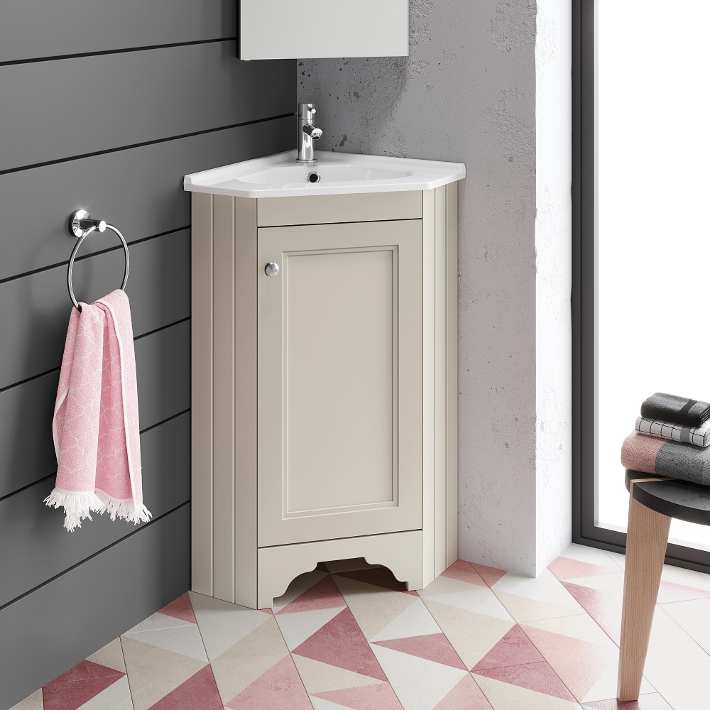 A charming vanity unit in chalk white with a curved front design and integrated basin. This space-saving piece is tastefully paired with a pink textured towel haging on a chrome ring holder and a stack of grey towels on a wooden stool, set against a playful geometric patterned floor in pink and beige tones. The bathroom exudes a soft, welcoming vibe accentuated by natural light streaming in from the side window. 
