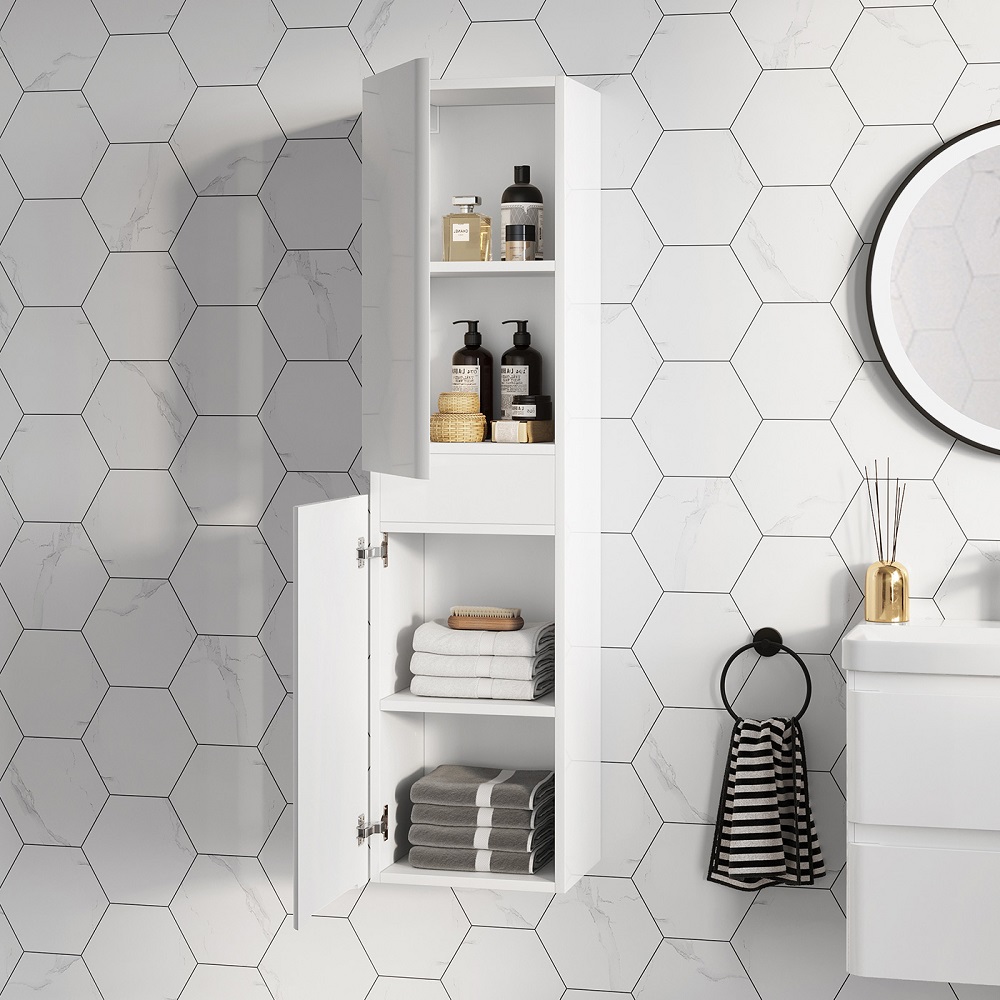 A tall, wall-hung bathroom cabinet in gloss white, with its door ajar revealing neatly organised shelves stocked with luxury toiletries, plush towels, and woven baskets. This elegant storage solution is mounted on a wall with distinctive hexagonal tiles that mimic marble, enhancing the clean and sophisticated feel of the space. A striped black and white hand towel hangs on a circular hook below, adding a touch of graphic charm to the scene. A round mirror and gold accents, including a reed diffuser, add a touch of luxury and warmth to the crisp, modern decor. 