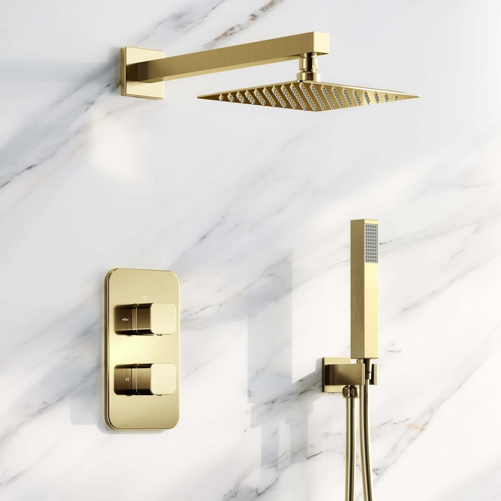 Brushed brass square thermostatic shower set against a white marble wall, including a rainfall shower head and a handheld sprayer with rectangular nozzles.