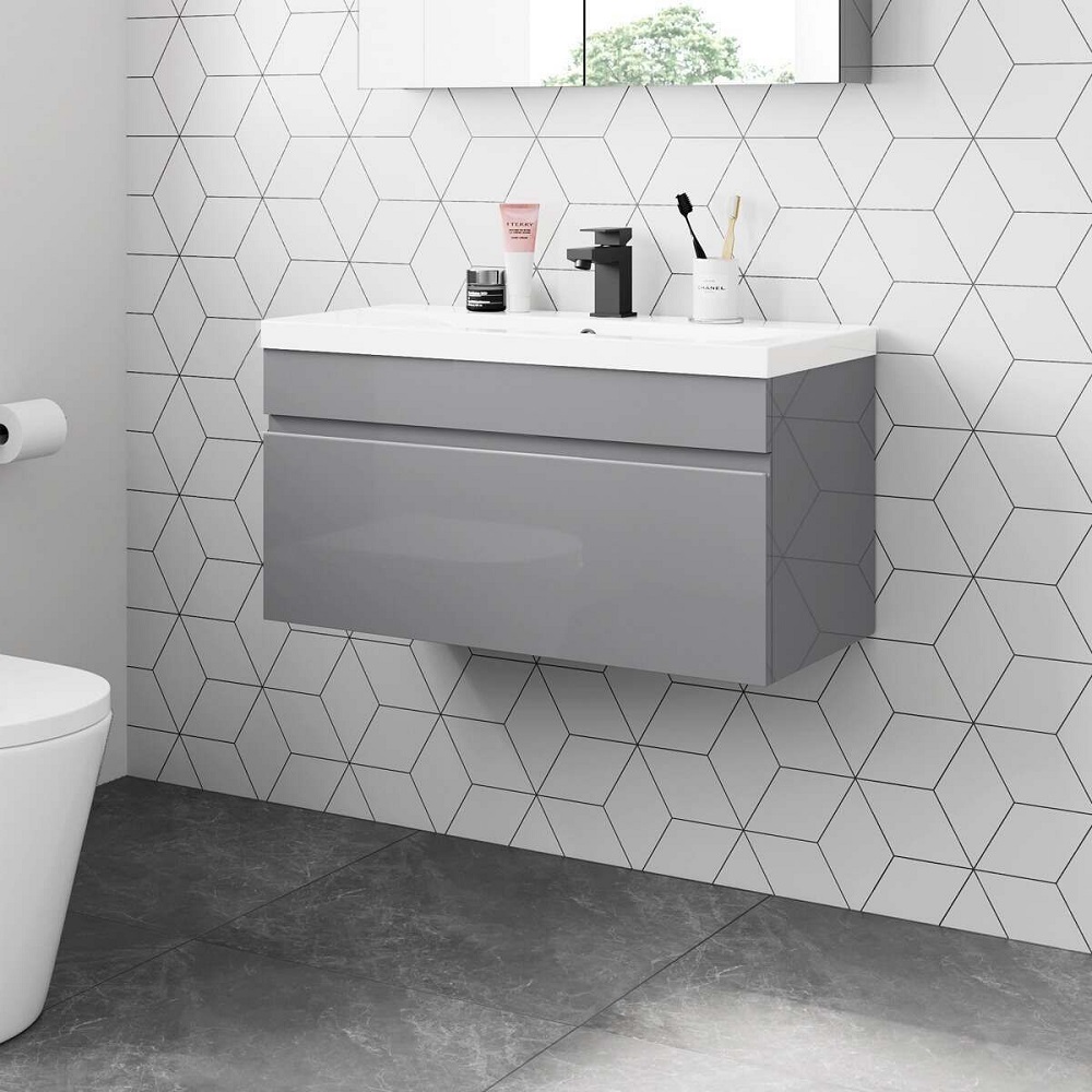 A minimalist and modern bathroom design featuring an 800mm Trent pebble grey wall-hung basin drawer vanity. The vanity boasts a smooth front and a spacious countertop sink, paired with a matt black faucet, offering a sleek and contemporary answer to the question " what is the best sink for the bathroom?" The geometrically patterned white wall tiles provide a dynamic backdrop, while the dark floor tiles anchor the space with a contrasting tone. This vanity unit is a perfect blend of form and function for any stylish bathroom interior. 